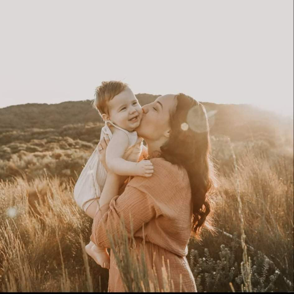 Mother kissing and holding up her baby boy with a mountain and plants in the background