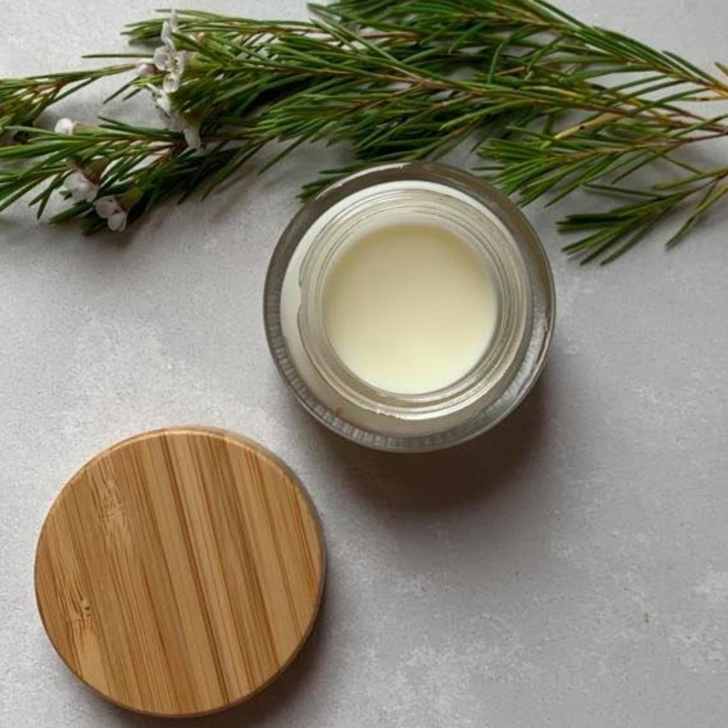 A bamboo and glass re-useable jar with lid off showing a natural cream essential oil multipurpose balm for adults, babies and children.