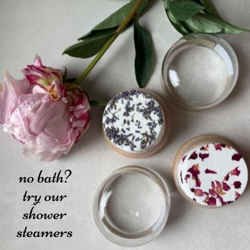 125g bamboo and glass reusable jars with lids off, containing 1 "slumber" shower steamer with lavender petals on top and 1 "just breathe" shower steamer with rose petals on top.